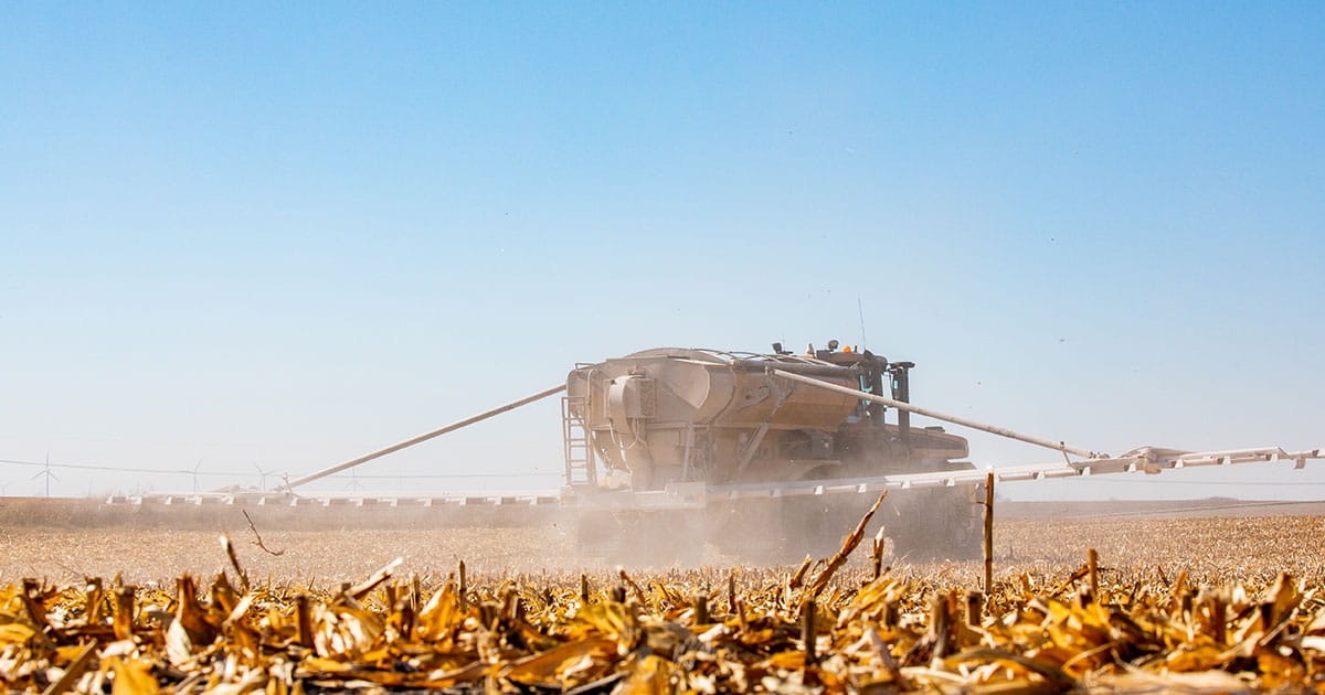 A dry fertilizer spreader in action in a harvested corn field.